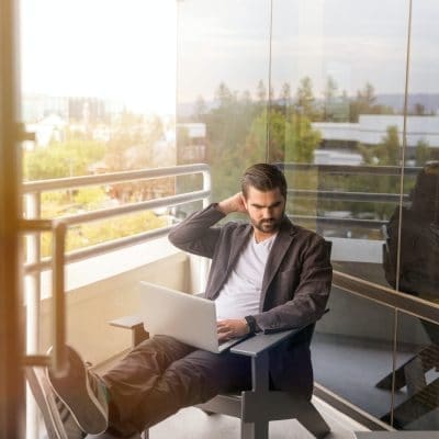 A man sitting on a balcony looking at his laptop